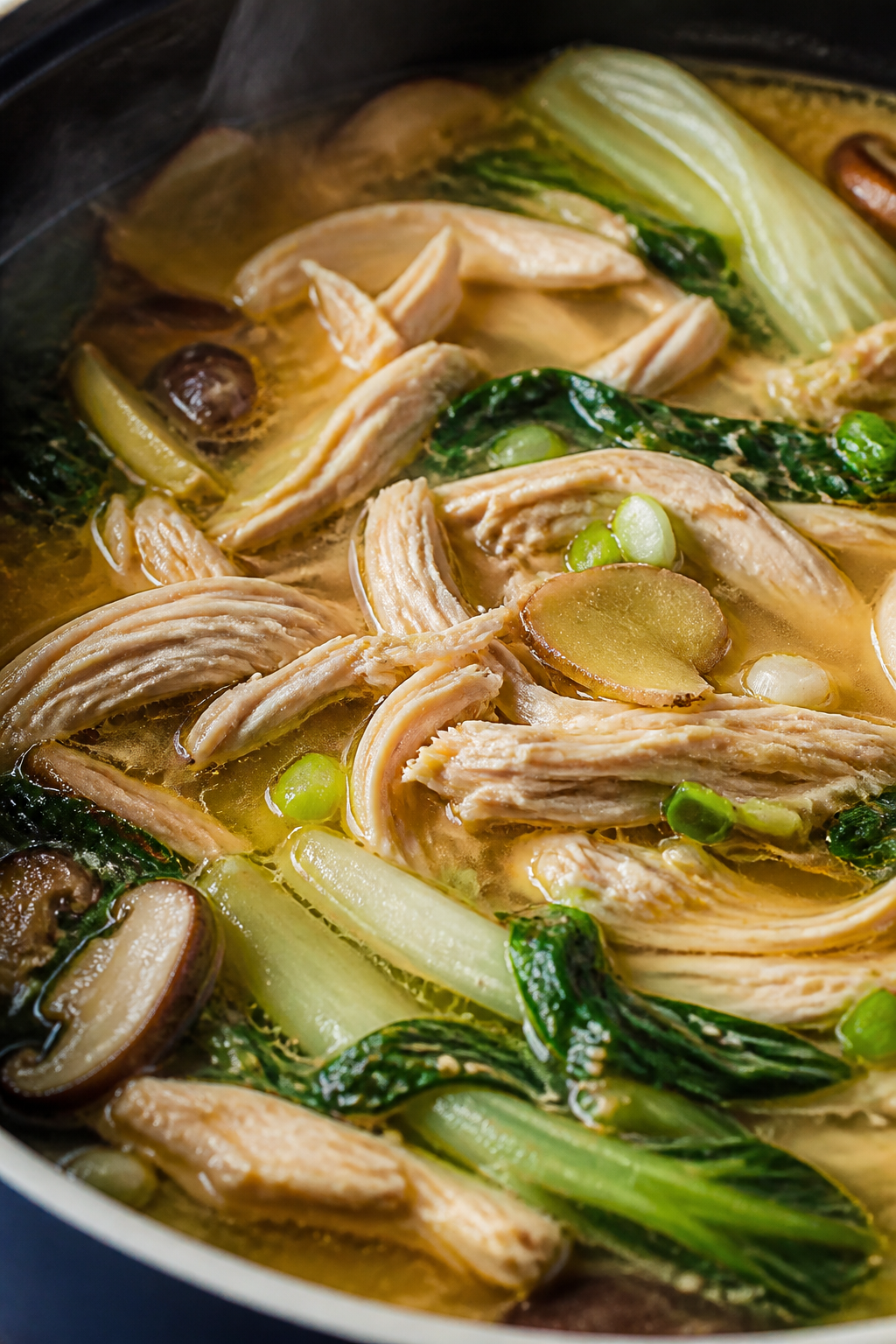 Close-up detail: Shredded sesame-ginger chicken just returned to a simmering golden broth with mushr