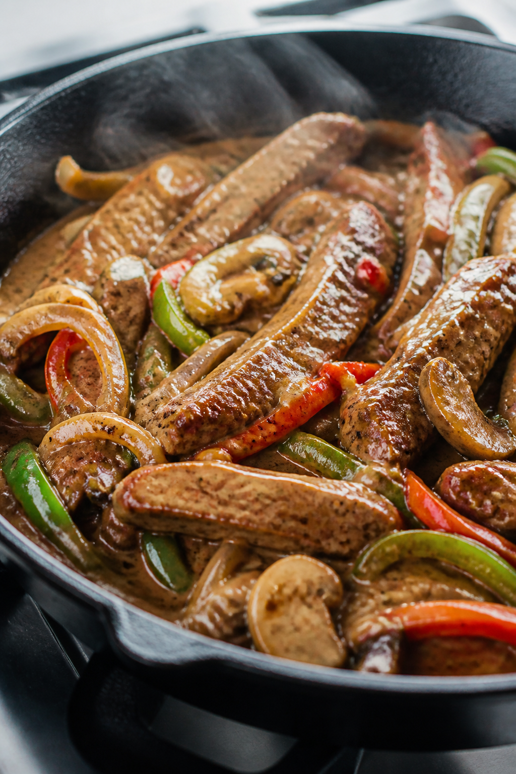 Close-up detail: Sizzling seared ribeye strips with caramelized peppers, onions, and mushrooms in a 