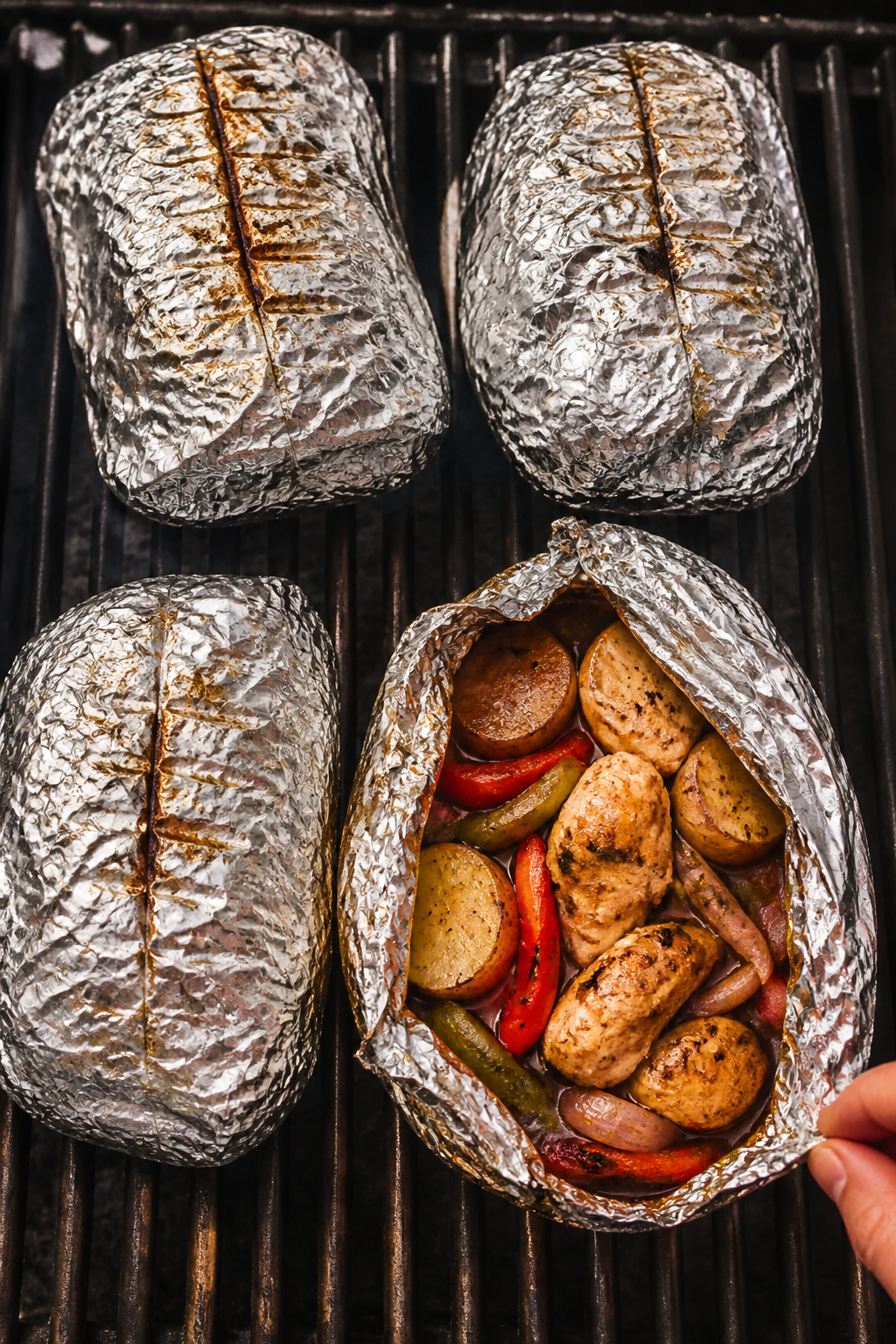 Cooking process: Overhead shot of four sealed heavy-duty foil packets on a grill at medium-high heat