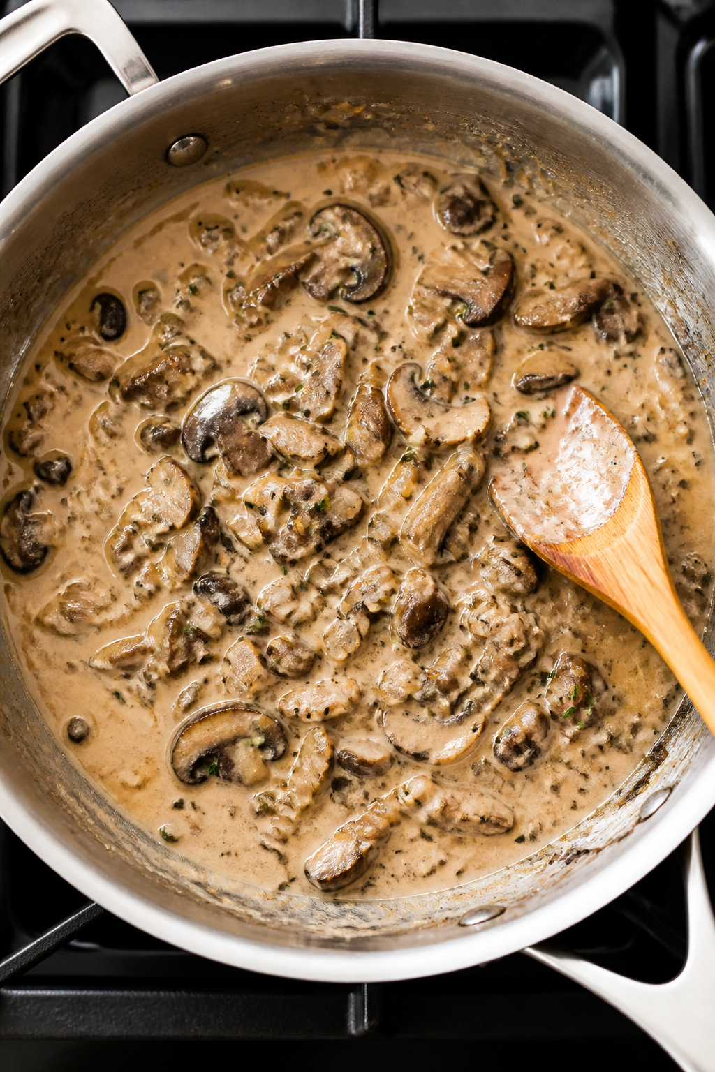 Cooking process: Overhead shot of the creamy mushroom sauce in a wide stainless skillet mid-simmer, 