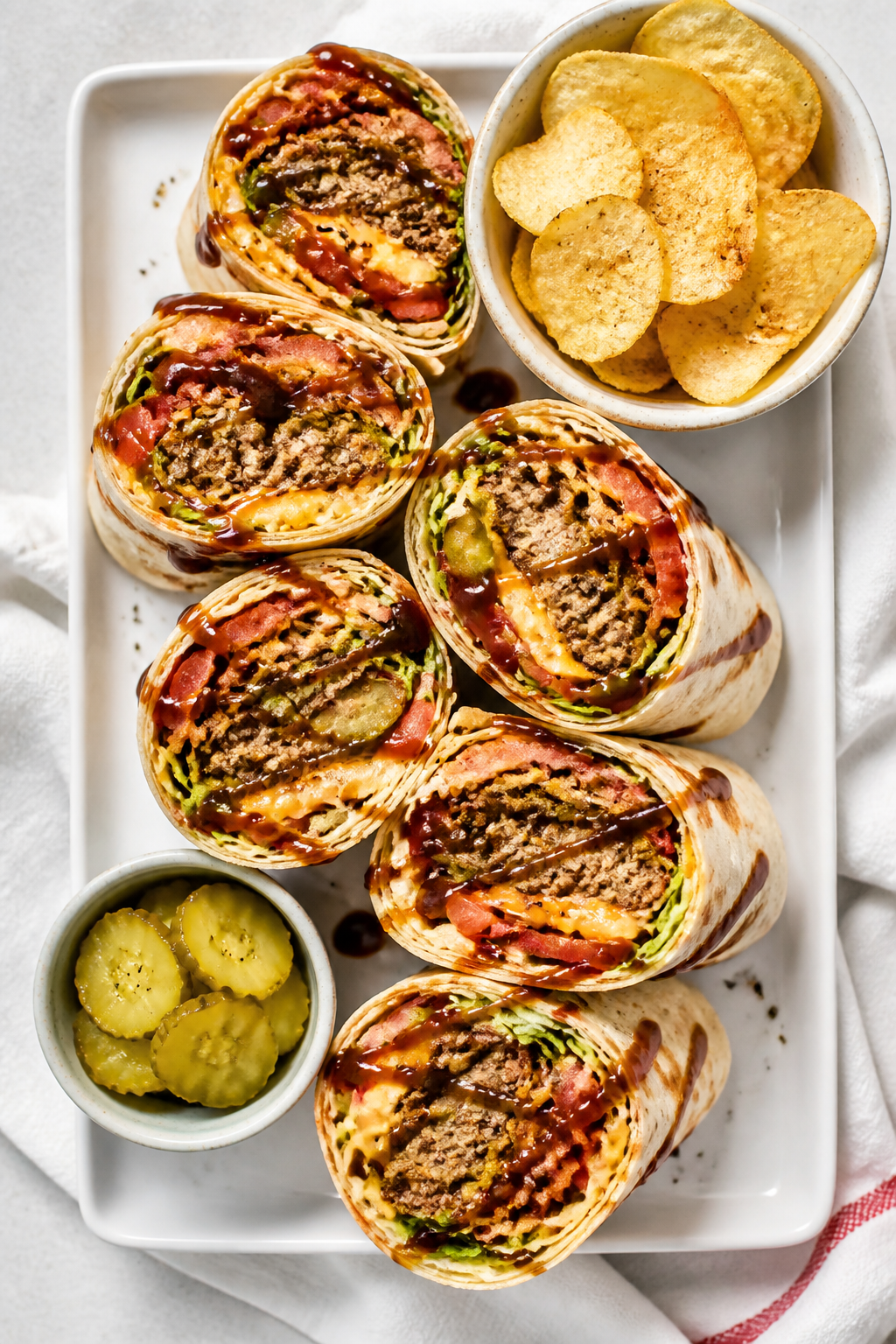 Tasty top view final presentation: Overhead platter of halved BBQ Bacon Cheeseburger Wraps arranged 