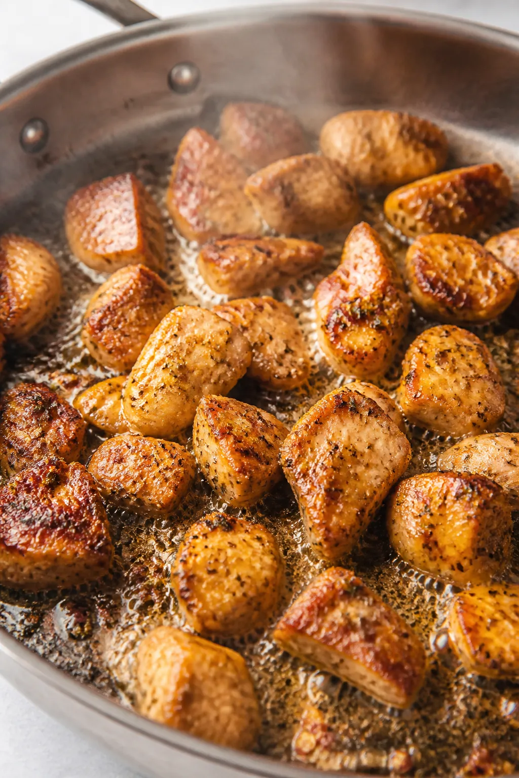 Cooking process, close-up: Golden-seared chicken bites sizzling in a large skillet with melted butte