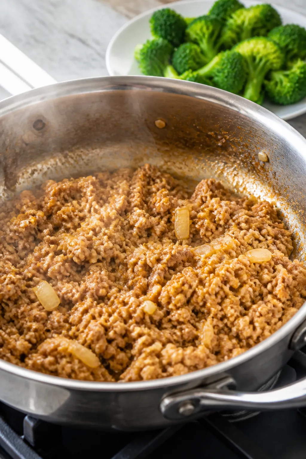 Cooking process close-up: Ground chicken browning in a large stainless steel skillet with diced yell