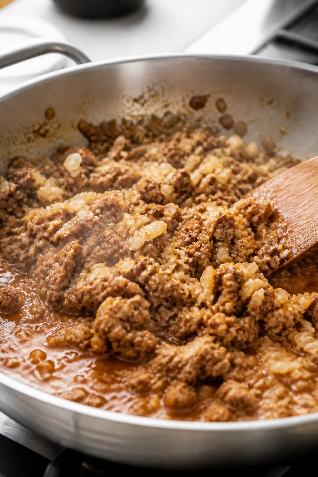 Cooking process close-up: Lean ground beef browning in a stainless skillet with diced yellow onions 