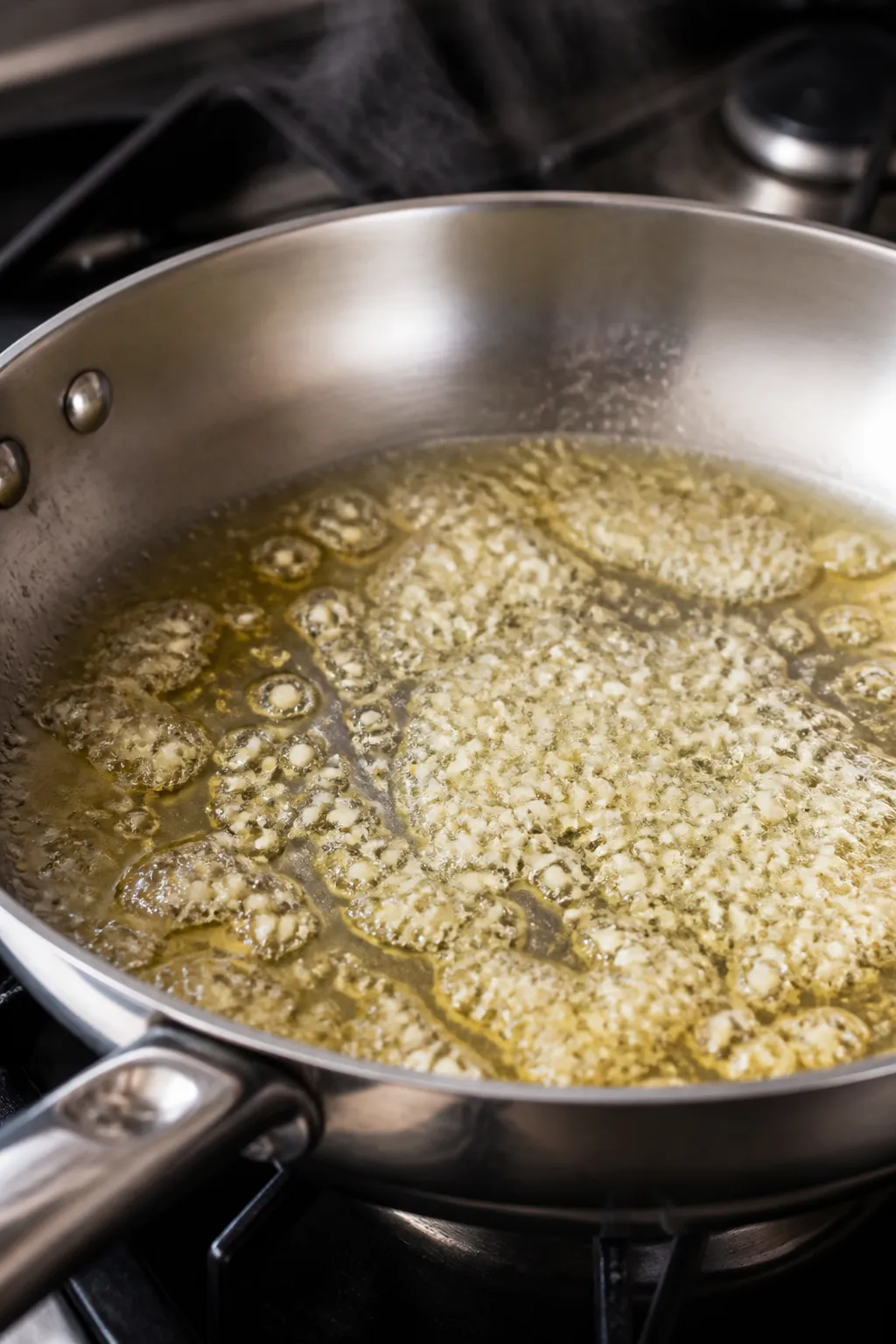 Cooking process close-up: Melted butter and minced garlic gently sizzling in a stainless skillet ove
